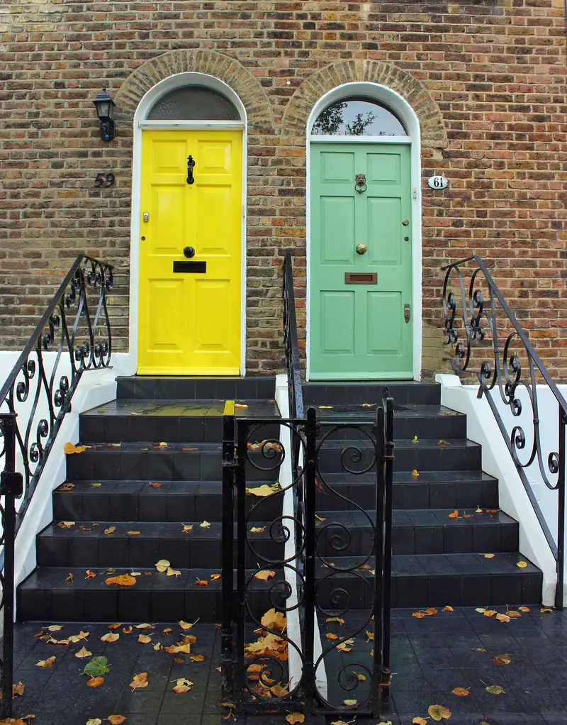 A yellow and a mint-green front door side by side at the top of black-railed steps